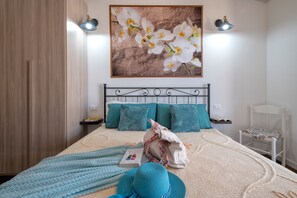 A bedroom with a bed, pillows, a nightstand, a reading lamp, a chair, and a wall-mounted painting.
