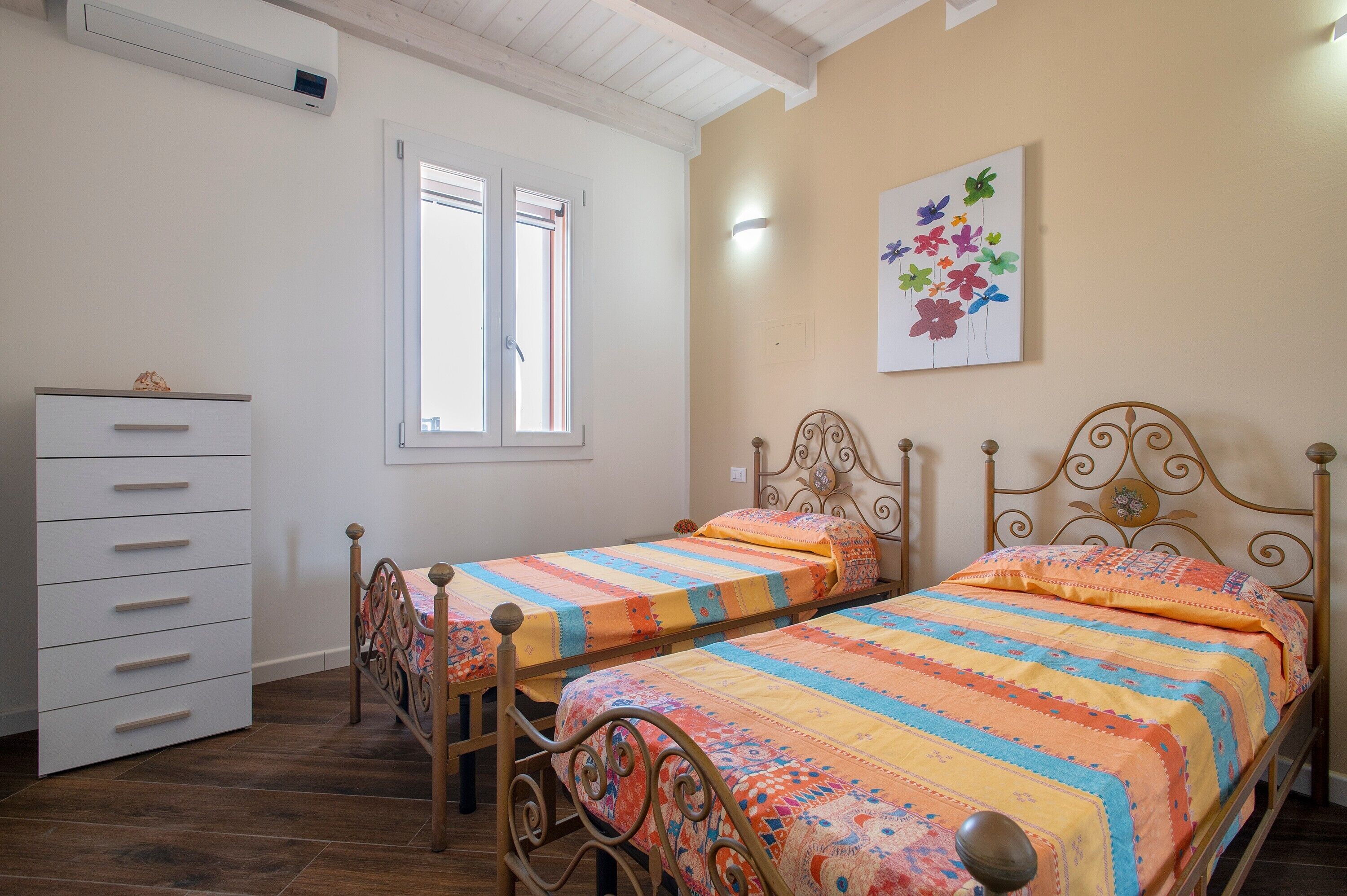A bedroom with two beds, a dresser, a window, and a wall-mounted artwork.
