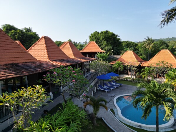 Un resort con varias edificaciones tipo bungalow, una piscina y abundante vegetación.