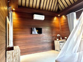 A room with wooden walls, a mounted TV, an air conditioning unit, a small table with a vase, and a bed with a canopy.