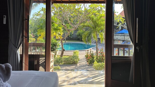 An open doorway to a pool area with a view of a swimming pool, surrounded by greenery and a stone wall. - Villa Vilah (Penida Island)