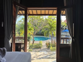 An open doorway to a pool area with a view of a swimming pool, surrounded by greenery and a stone wall.