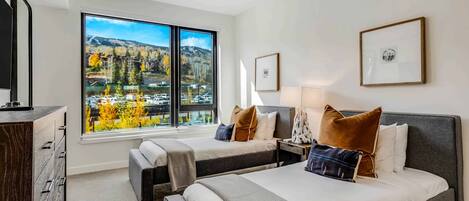 Ett hotellrum med två sängar, ett stort fönster med utsikt över bergen, en takfläkt och inramade tavlor på väggen.