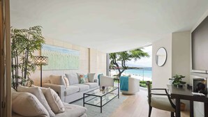 Un salon moderne avec un canapé, une table basse et un coin repas. De grandes fenêtres offrent une vue sur l’océan.
