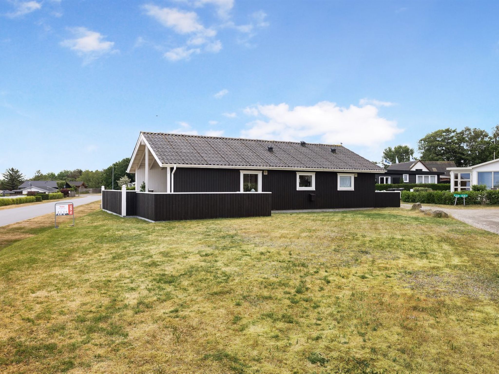 Ett envåningshus med en mörk fasad, ett sluttande tak och en liten trädgård framför huset.