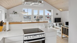 A modern kitchen with a white countertop, a stove, and an oven. There is a window with a view of houses outside.