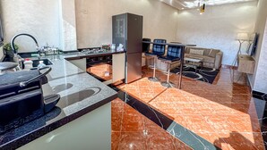 A modern kitchen with a built-in stove, a refrigerator, and a dining area with two bar stools. - El-wifaq - Appartement 2 (Agadir)