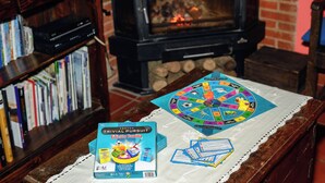 A cozy room with a fireplace, a bookshelf, and a table with a board game and a game box. - Casa Rural en la Montaña de León. Entre Valles (Benllera)