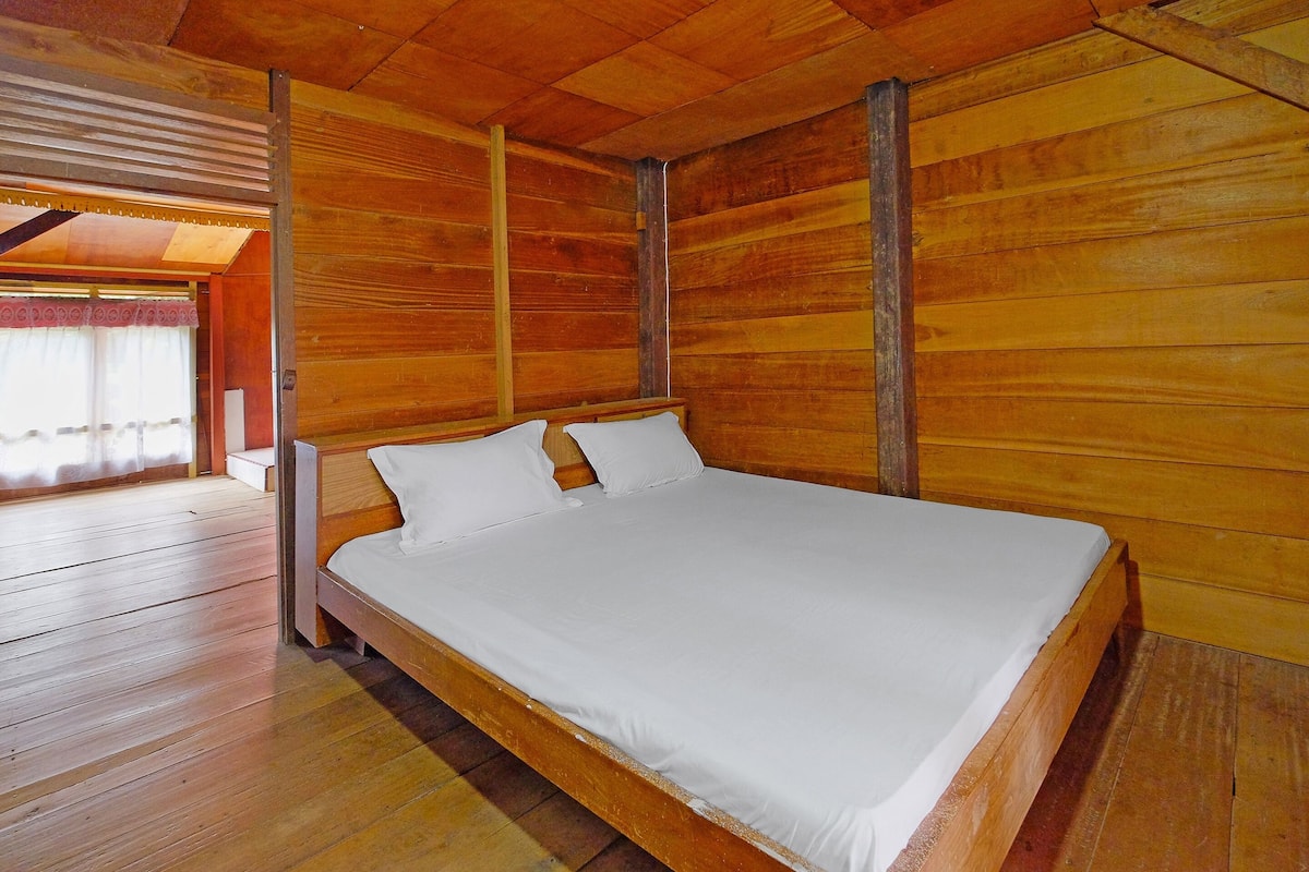 Una habitación de madera con una cama, paredes de madera y un ventanal con cortinas.