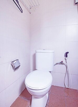 A white toilet with a tank, a wall-mounted hand dryer, and a visible water pipe.