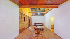 Quarto com piso de madeira, uma mesa redonda com cadeiras e teto inclinado com vigas de madeira.