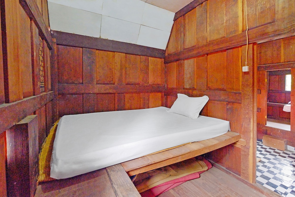 Una cama individual en una habitación con paneles de madera y suelo a cuadros.