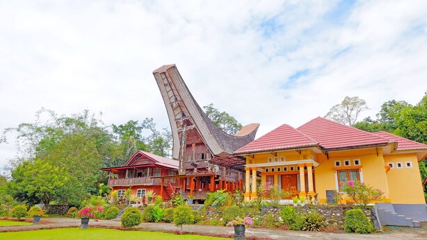 Uma casa de madeira tradicional com telhado íngreme, rodeada por vegetação exuberante e um jardim bem cuidado.