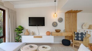 A modern living room with a flat-screen TV, wooden shelves, a wicker chair, and a large window. - San Lameer Villa 3009 (Southbroom)