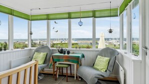 Ein gemütliches Zimmer mit Meerblick, ausgestattet mit einem Tisch mit Stühlen, einem Fenster mit grünen Jalousien und einer Hängelampe.