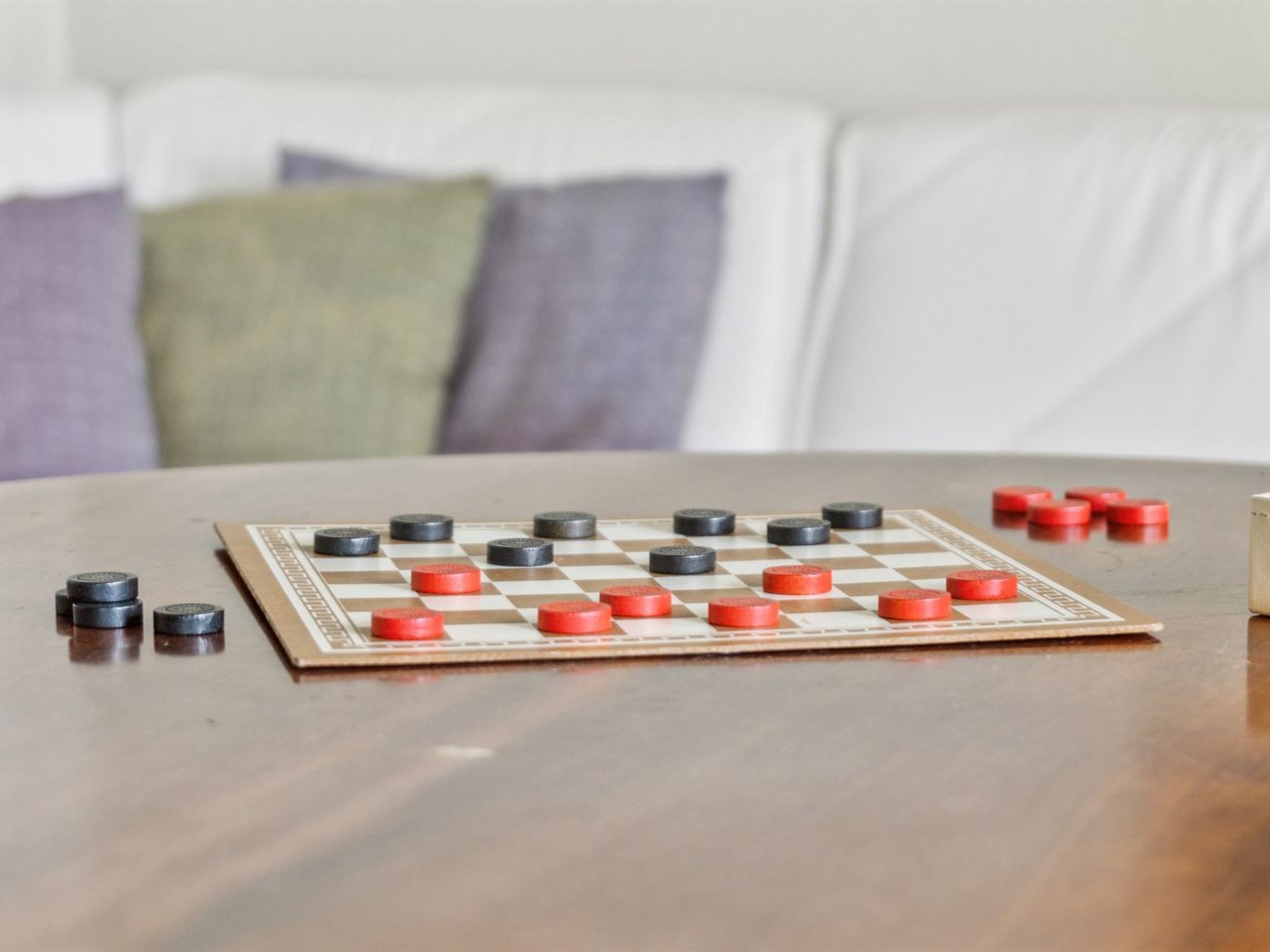 Un gioco da tavolo a scacchi con pedine su un tavolo di legno, posizionato su un divano con cuscini.