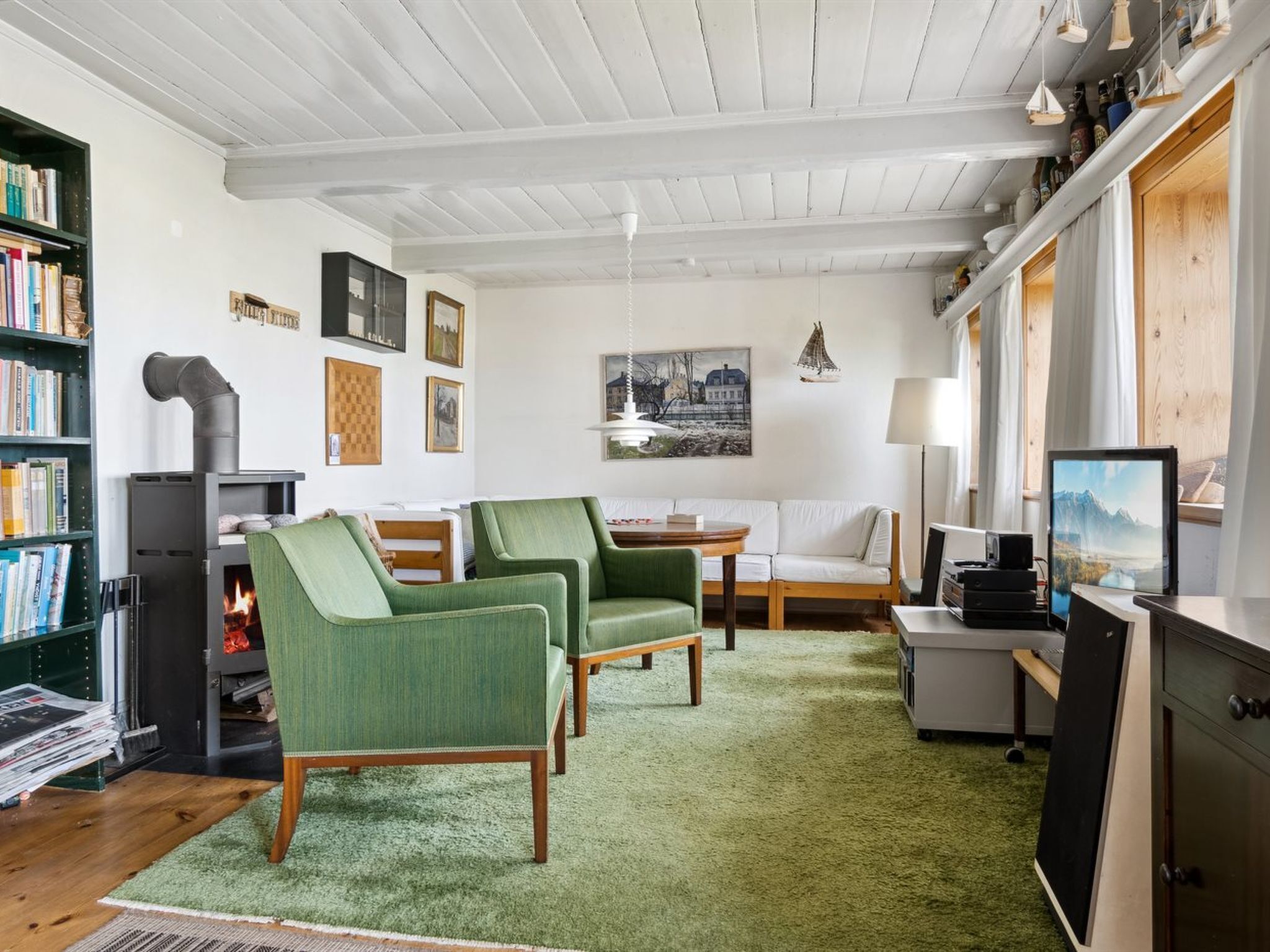 Un salon chaleureux avec une cheminée, des fauteuils verts, un canapé blanc et une bibliothèque.