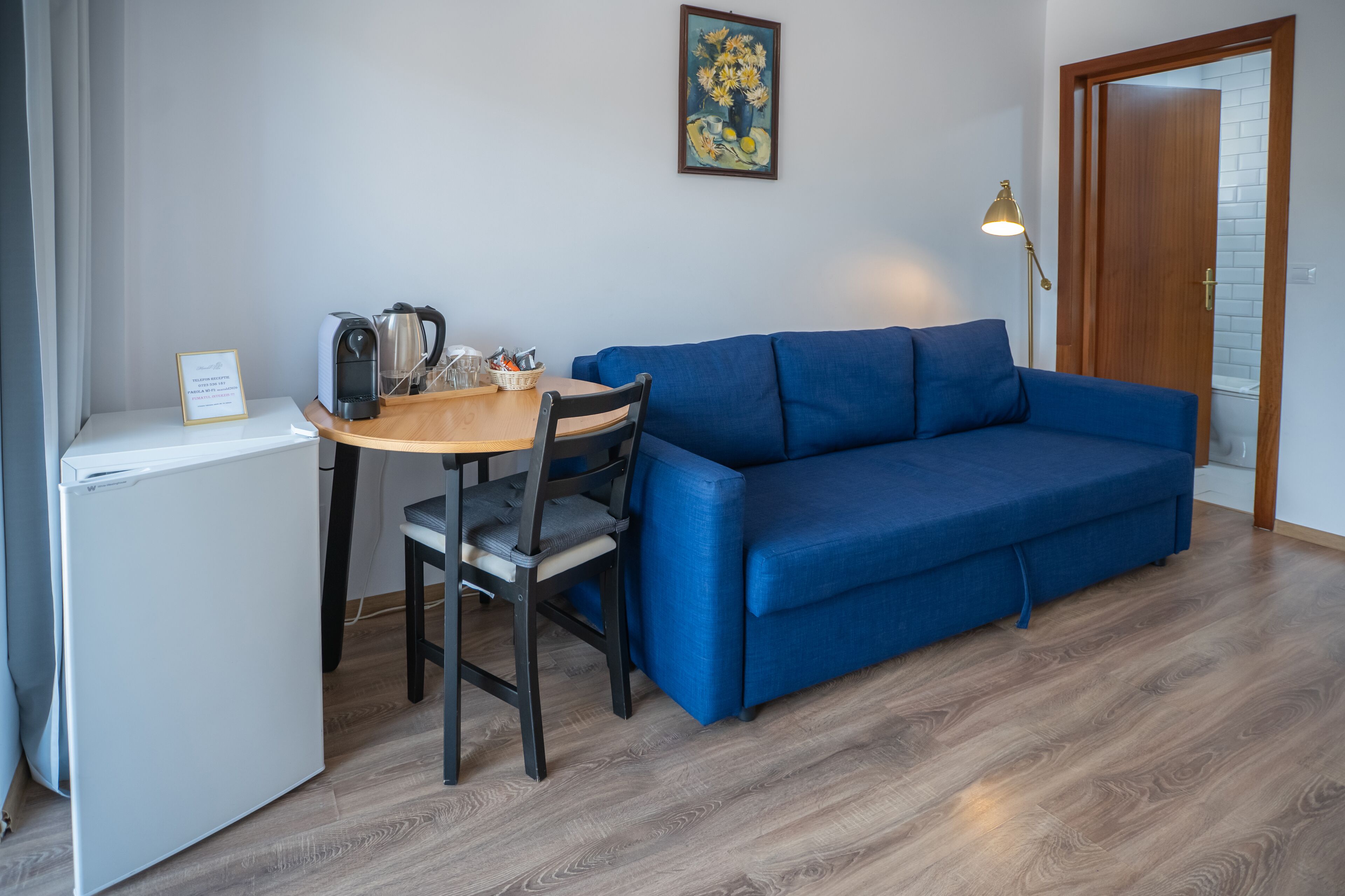 A compact living space with a blue sofa, a wooden dining table, a coffee maker, and a small white refrigerator.