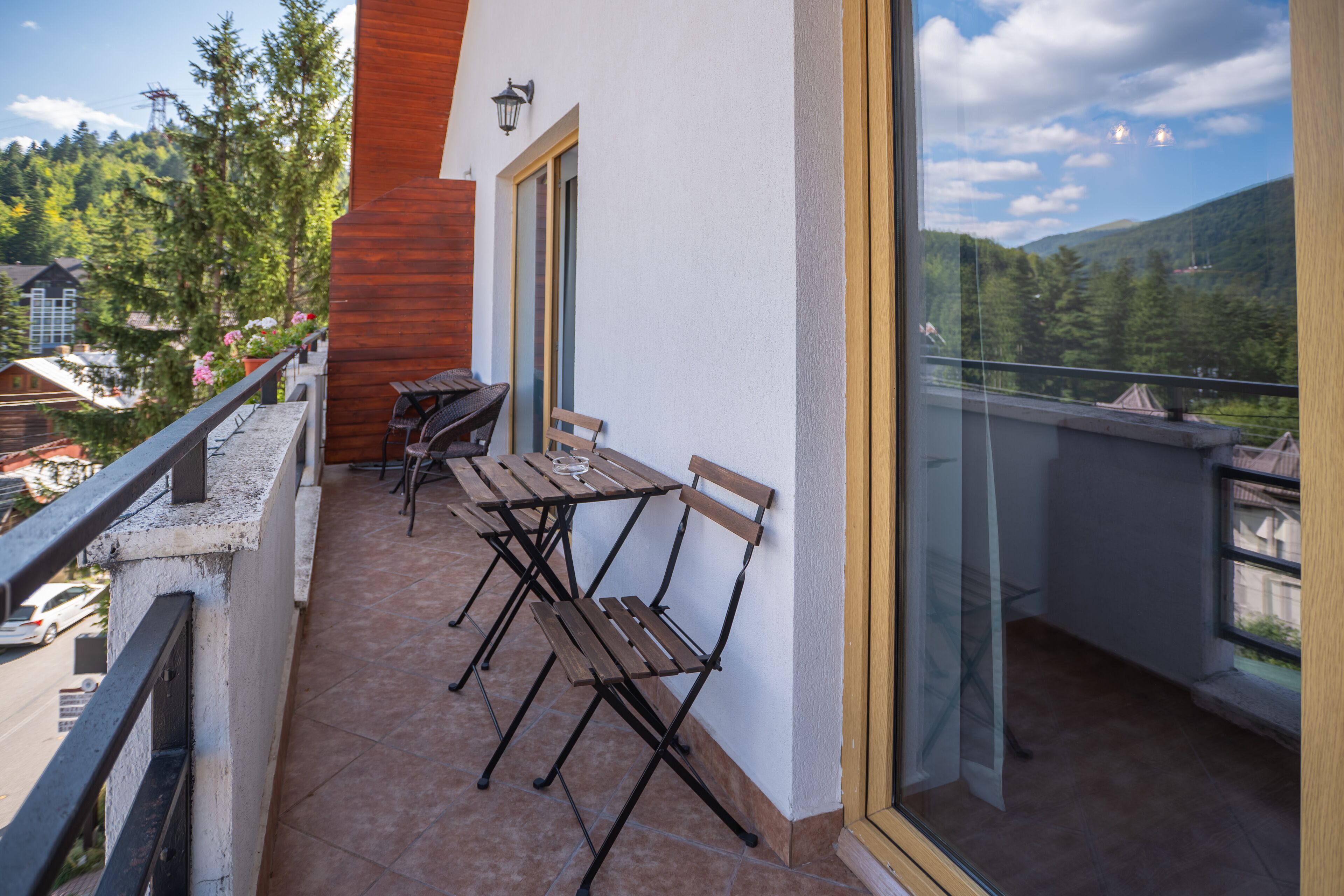 Un balcon avec une table et des chaises en bois, une balustrade en verre et une vue sur un paysage montagneux.