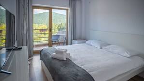 Habitación de hotel con una cama grande, televisión, balcón con vistas a la montaña y una silla.