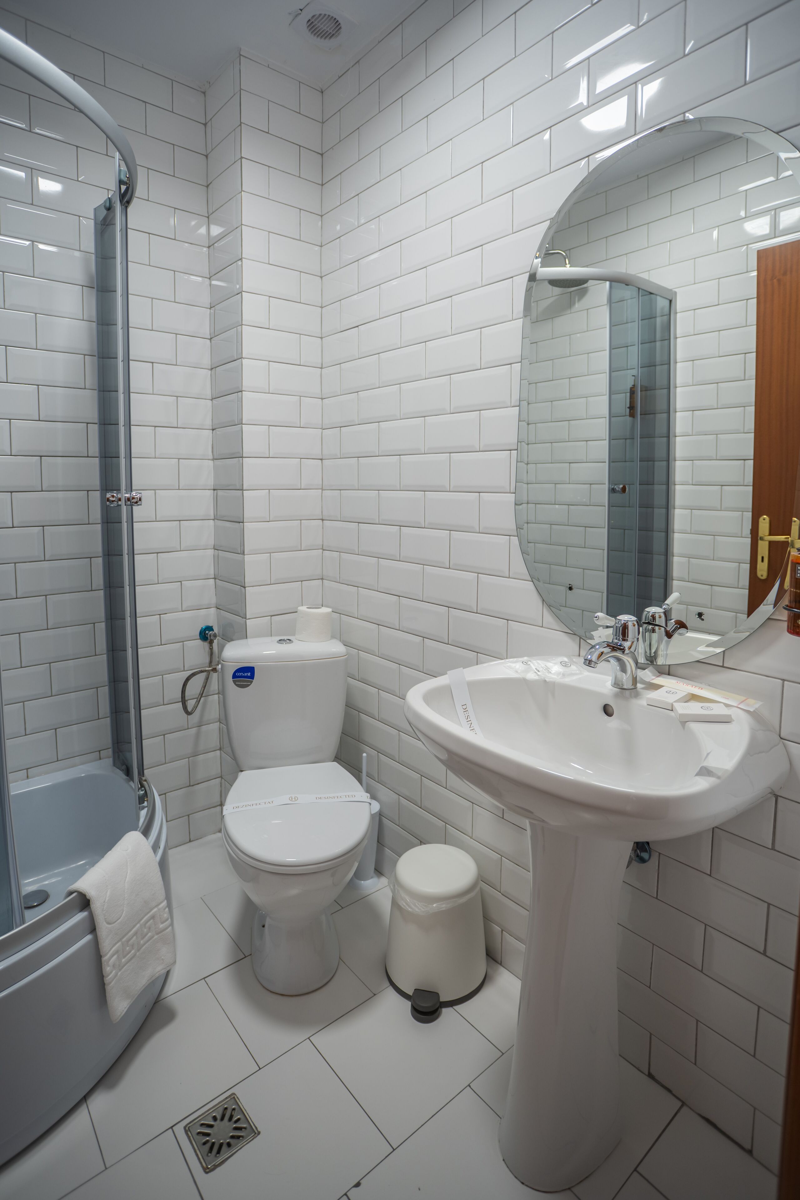 Een moderne badkamer met witte tegels, een douchecabine van glas, een toilet, een wastafel en een spiegel.
