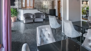 Un moderno hall de hotel con una zona de estar central, una escalera y un gran espejo que refleja el interior.