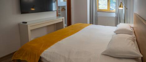 A modern hotel room with a large bed, a TV mounted on the wall, a bedside table, and a window with curtains.