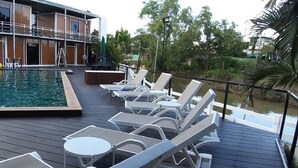 A deck with lounge chairs and tables, a pool, and a building in the background. - Hi Creek Resort  (Si Bun Rueang)