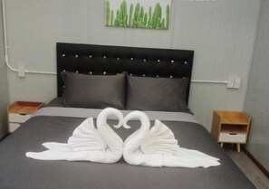 Un letto con una testiera nera, biancheria grigia e due asciugamani bianchi disposti a forma di cigno.