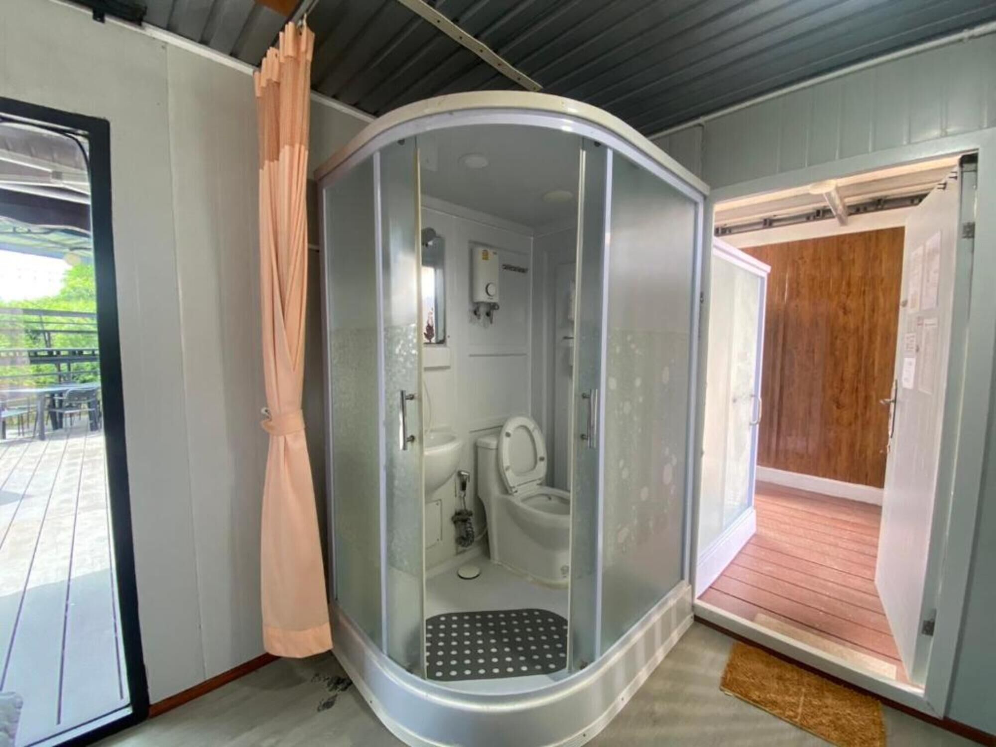 Casa de banho compacta com cabine de duche de vidro, sanita, chuveiro e um lavatório pequeno.
