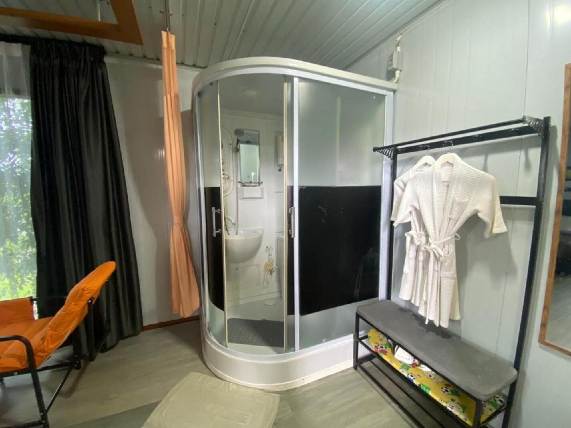 A bathroom with a glass-enclosed shower, a sink, and a towel rack with robes.