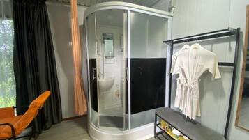 A bathroom with a glass-enclosed shower, a sink, and a towel rack with robes.