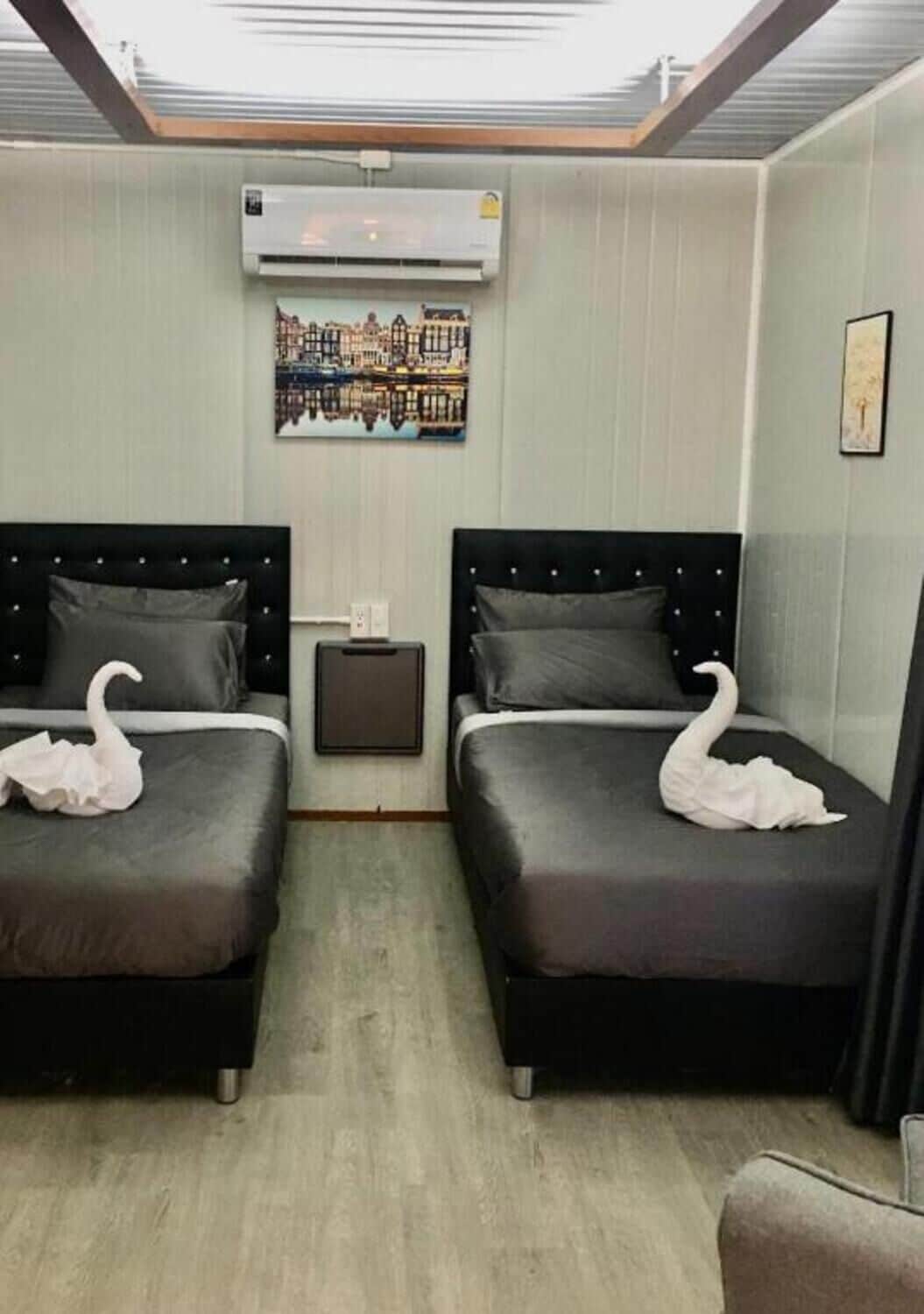 A hotel room with two beds, an air conditioning unit, a painting, and a small table.