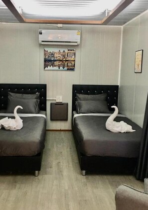 A hotel room with two beds, an air conditioning unit, a painting, and a small table.
