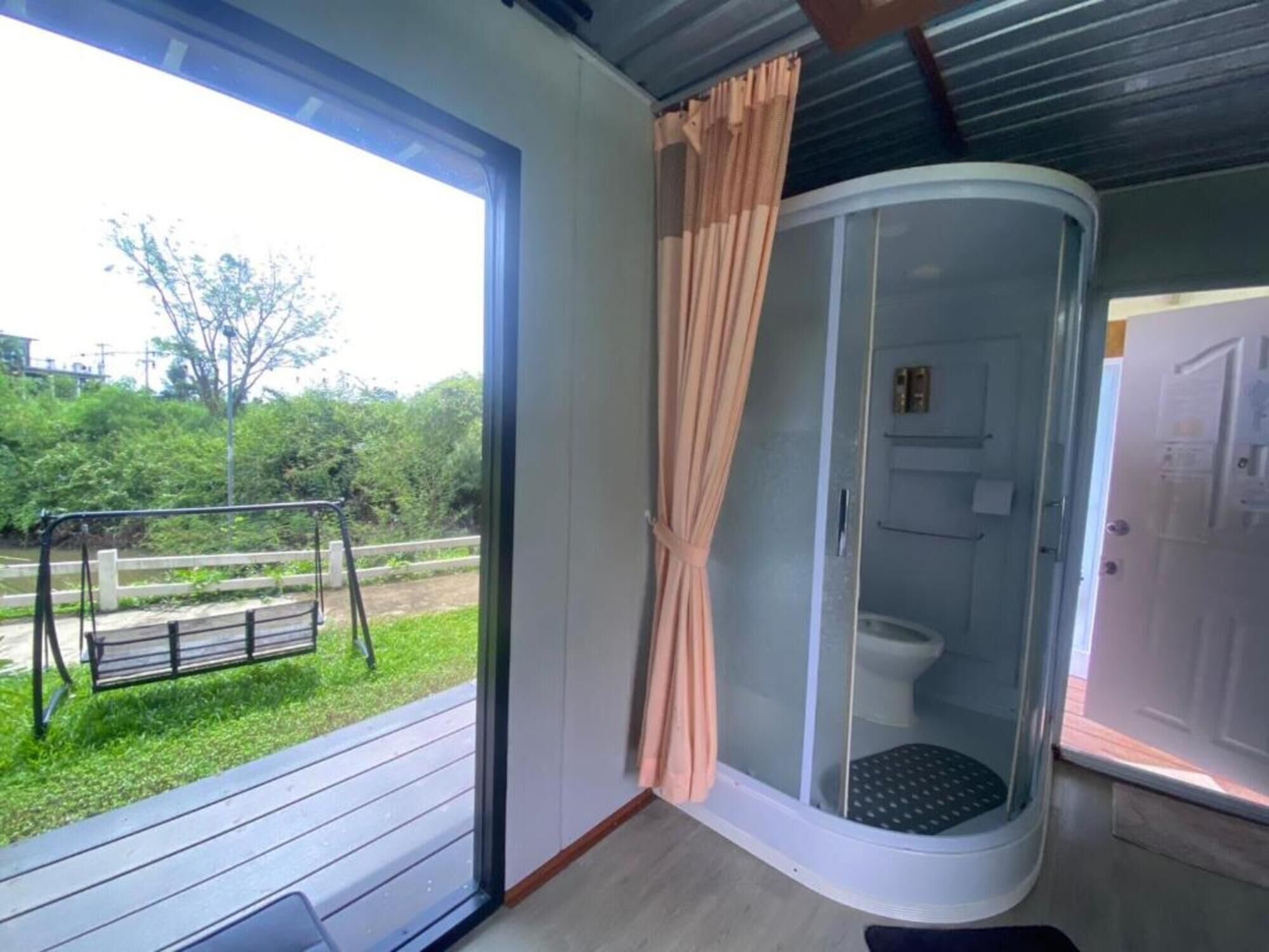 A room with a glass shower enclosure, a swing set outside, and a view of greenery.