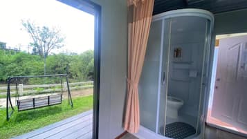 A room with a glass shower enclosure, a swing set outside, and a view of greenery.