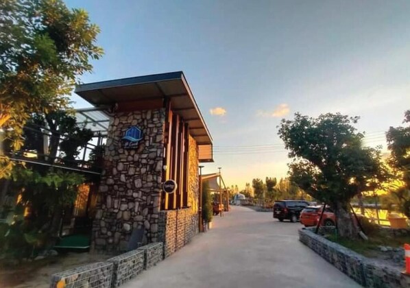 Un bâtiment en pierre avec une enseigne, un chemin pavé et des voitures garées.