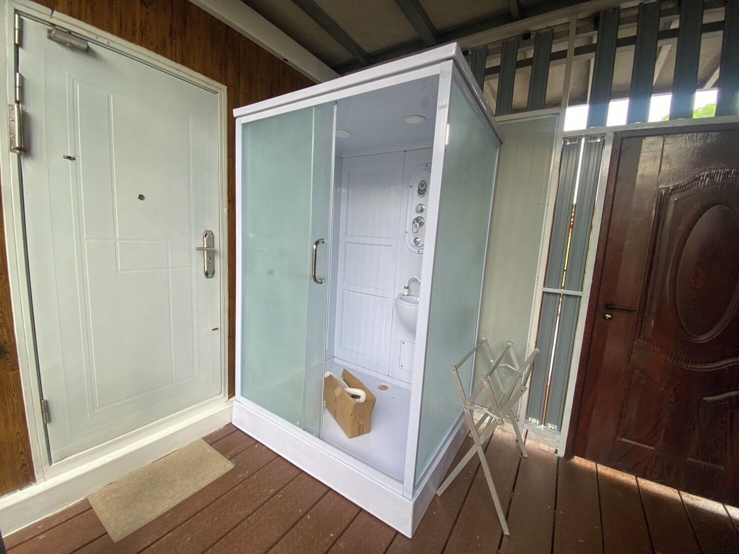 A room with a glass-enclosed shower, a wooden door, and a small folding chair.