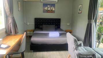 A bedroom with a bed, bedside tables, a desk, a chair, an air conditioning unit, and a window with curtains.