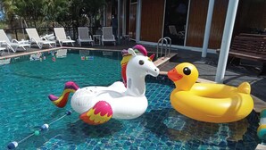 A swimming pool with inflatable unicorn and duck floats, surrounded by lounge chairs and a wooden deck. - Hi Creek Resort  (Si Bun Rueang)