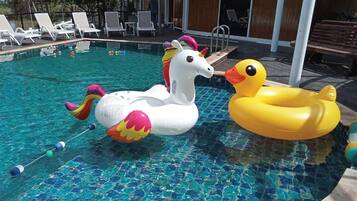 Una piscina con flotadores de unicornio e pato inflables, rodeada de sillones de descanso y una terraza de madera.
