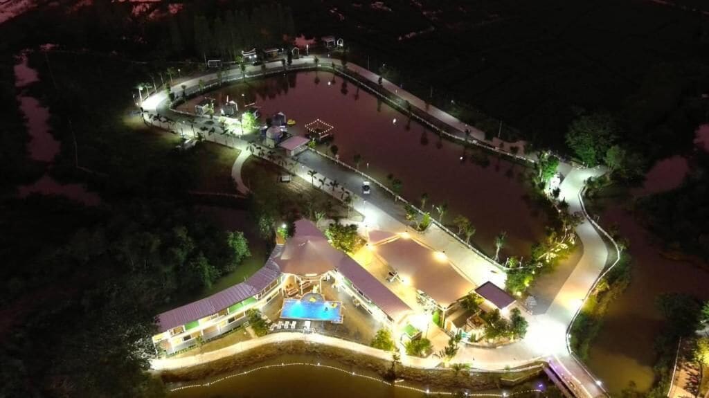 An aerial view of a waterfront property with a swimming pool, a covered patio, and a road leading to the entrance.