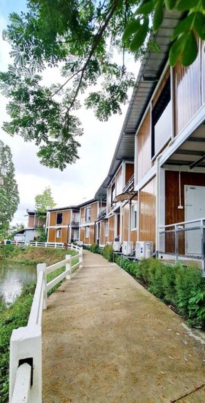 A row of wooden-framed buildings with large windows, a concrete pathway, and a body of water in the background.