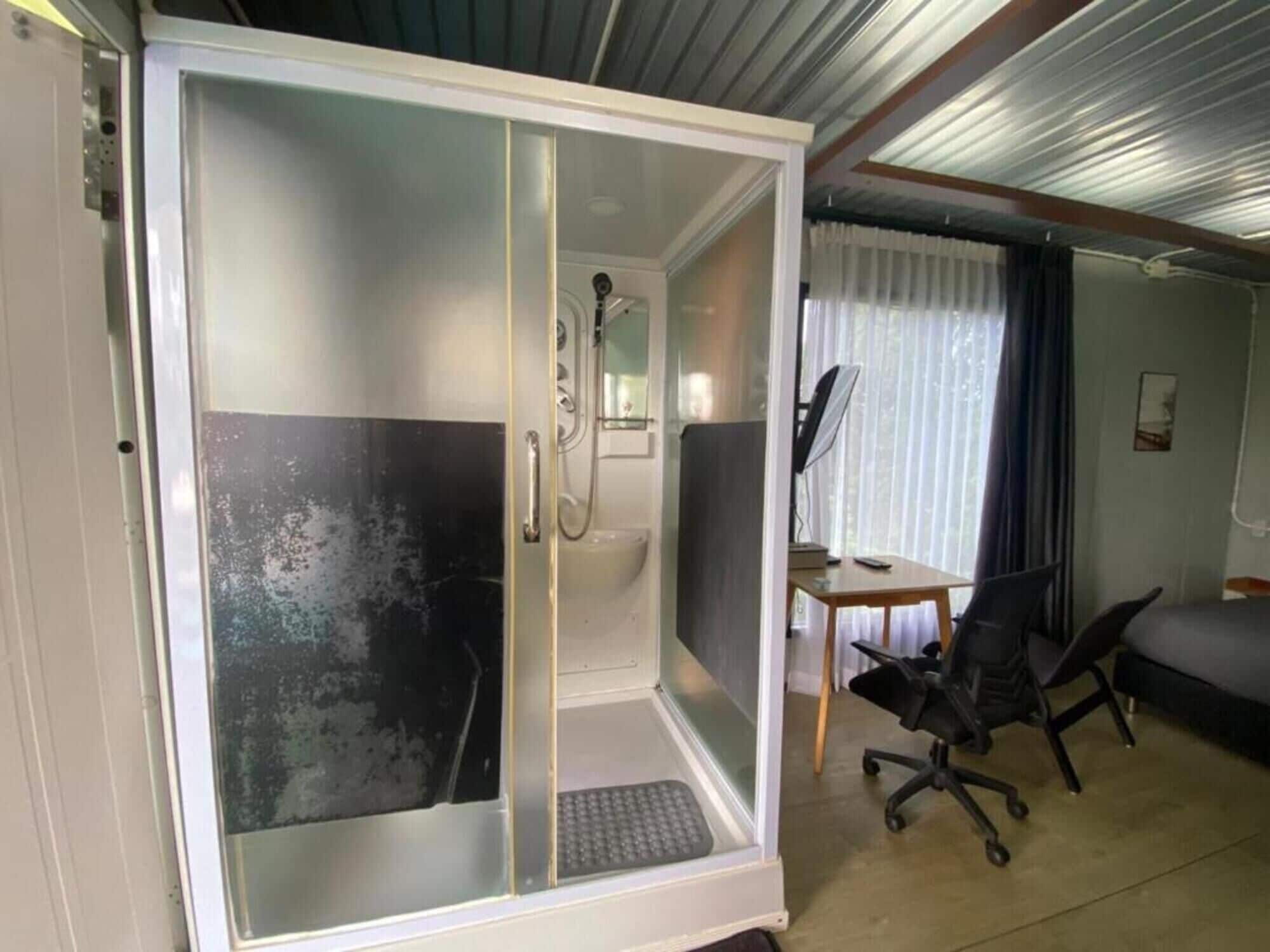 Une chambre dotée d’une cabine de douche, d’un bureau avec une chaise et d’un lit.
