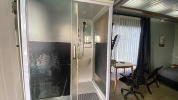 Une chambre dotée d’une cabine de douche, d’un bureau avec une chaise et d’un lit.