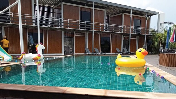 A swimming pool with inflatable toys, a slide, and a building with a wooden facade and balconies. - Hi Creek Resort  (Si Bun Rueang)