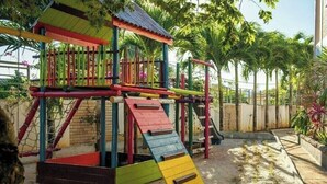 Värikäs leikkikenttä, jossa on liukumäkiä ja kiipeilytelineitä, ja jota ympäröivät palmut ja tiiliseinä.