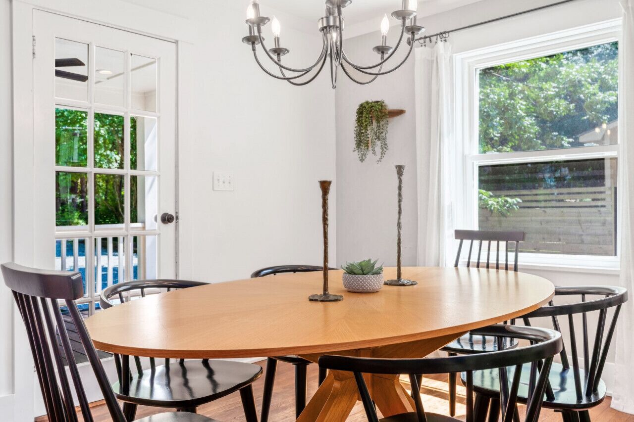 Un coin repas avec une table ronde en bois, des chaises noires, un lustre et une fenêtre donnant sur un paysage verdoyant.