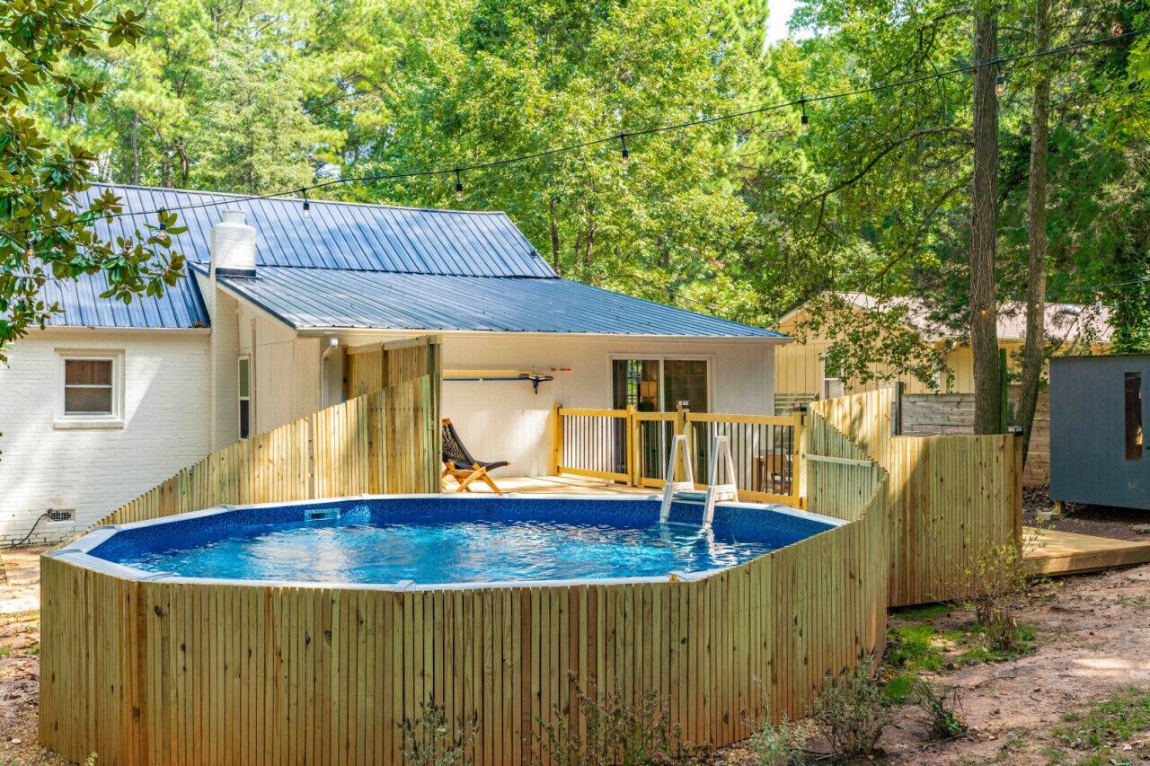 A backyard with a wooden deck, a swimming pool, and a house with a metal roof.