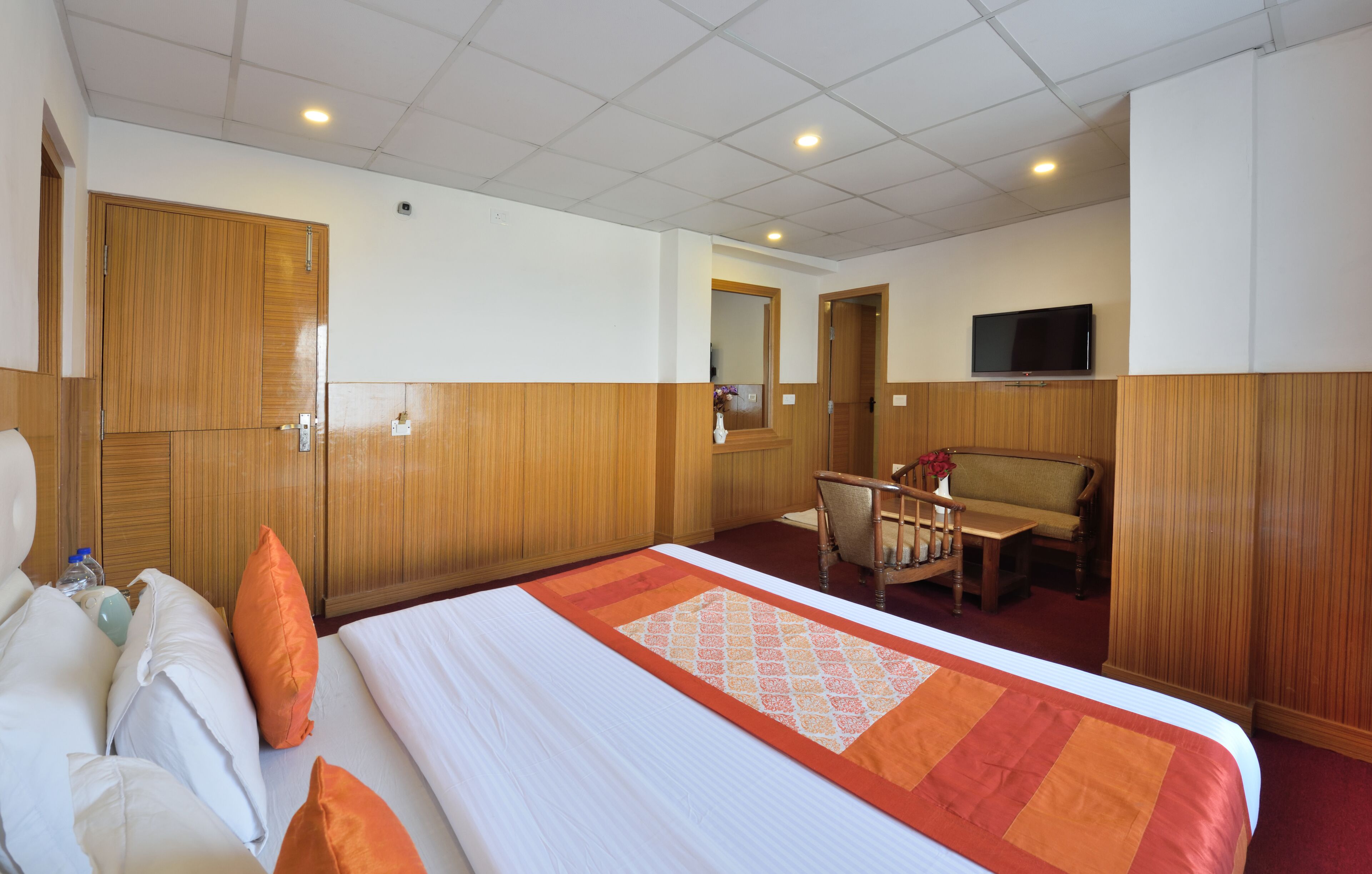Une chambre d’hôtel avec un grand lit, une armoire en bois, une télévision et un coin salon comprenant une chaise et une table.